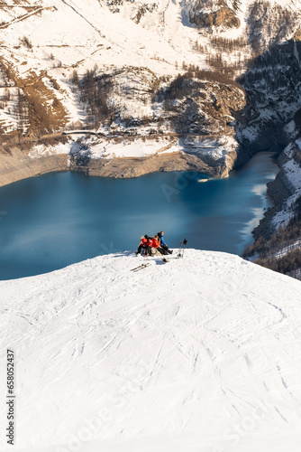 skiers resting on a mountaintop in front of a beautiful lake