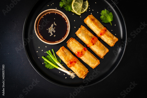 Vegetable filled spring rolls and soy sauce on black wooden table
