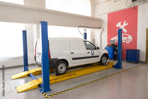 White van on a lift in a workshop, ready for servicing. Auto repair shop with a car on a lifting platform. Car in auto repair shop mechanical car repair at service station.