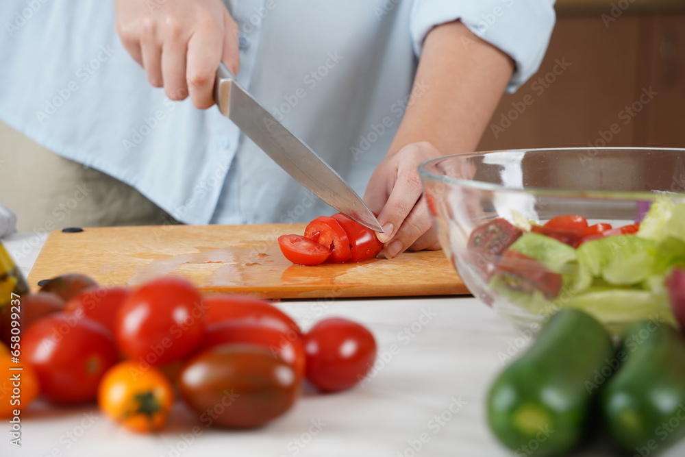 The woman in the process of making vegetable salad. Closeup of hands  cutting tomatoes on wooden table
