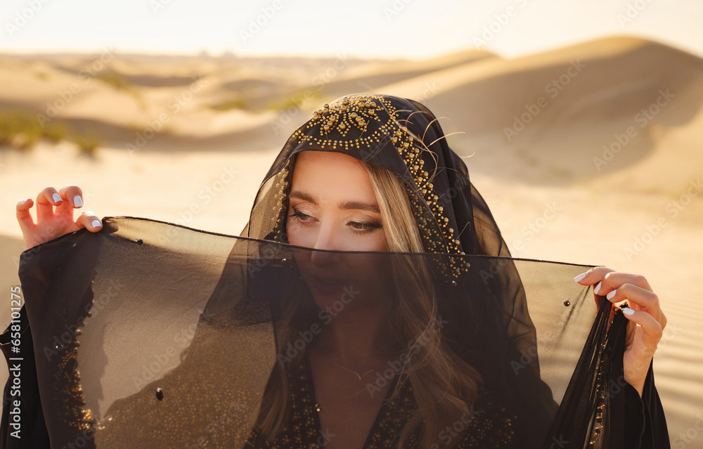 Desert adventure. Young arabian Woman posing in traditional Emirati dress abaya in sanddunes of UAE desert at sunset. The Dubai Desert Conservation Reserve, United Arab Emirates. - obrazy, fototapety, plakaty 
