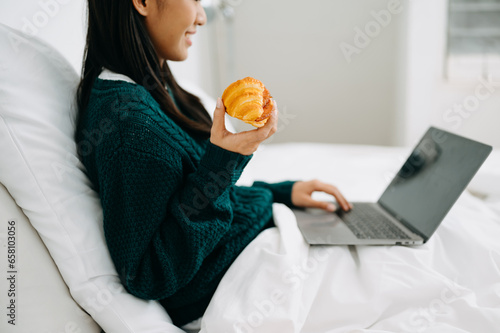 Canvas Print Beautiful young asian woman on a white bed with coffee cub and using smart phone at home