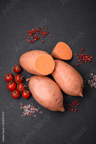 Fresh large pink sweet potato tubers with tomatoes and spices on a dark background