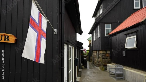 Gentle breeze blowing on Faroese flag on wooden exterior in Gasadalur, Vagar, Faroe Islands. Closeup