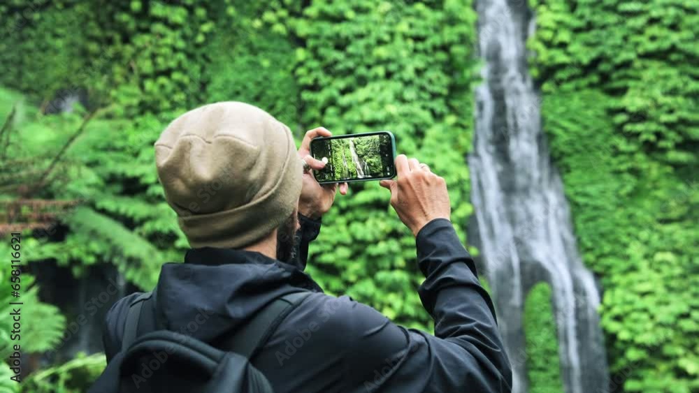 Adult Man Traveling in Green Nature Takes Phone Photo of Forest Waterfall. Lifestyle of Young Unrecognizable Person at Trip Destination of Jungle Water Fall. Concept of Traveler Making Journey Videos Adult Man Traveling in Green Nature Takes Phone Photo of Forest Waterfall. Lifestyle of Young Unrecognizable Person at Trip Destination of Jungle Water Fall. Concept of Traveler Making Journey Videos