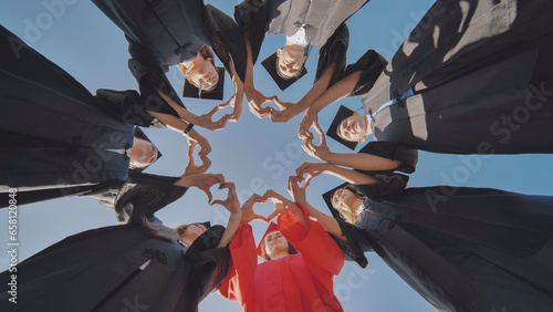 A group of seven college graduates make a heart shape from their hands while standing in a circle wearing robes.
