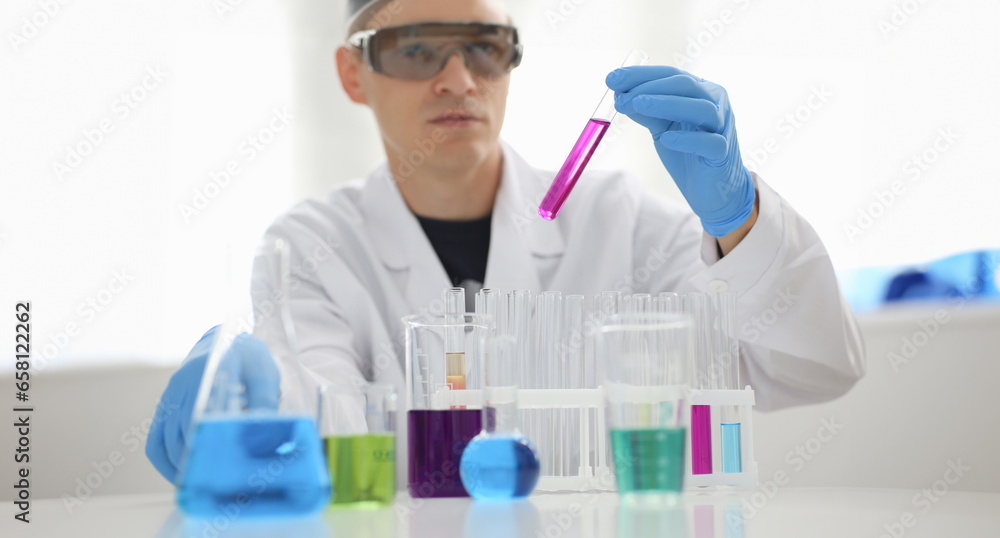 A male chemist holds test tube of glass in his hand overflows a liquid solution of potassium permanganate. Conducts an analysis reaction takes various versions of reagents using chemical manufacturing A male chemist holds test tube of glass in his hand overflows a liquid solution of potassium permanganate. Conducts an analysis reaction takes various versions of reagents using chemical manufacturing
