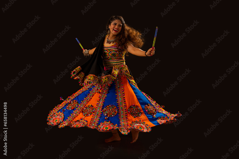 Gujarati woman dancing with dandiya sticks on a balck background, during Navratri Celebrations