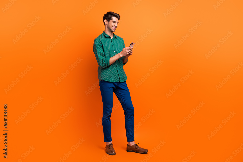Full body photo of young guy worker hr manager recruiter browsing swipe internet web pages smartphone isolated on orange color background Full body photo of young guy worker hr manager recruiter browsing swipe internet web pages smartphone isolated on orange color background