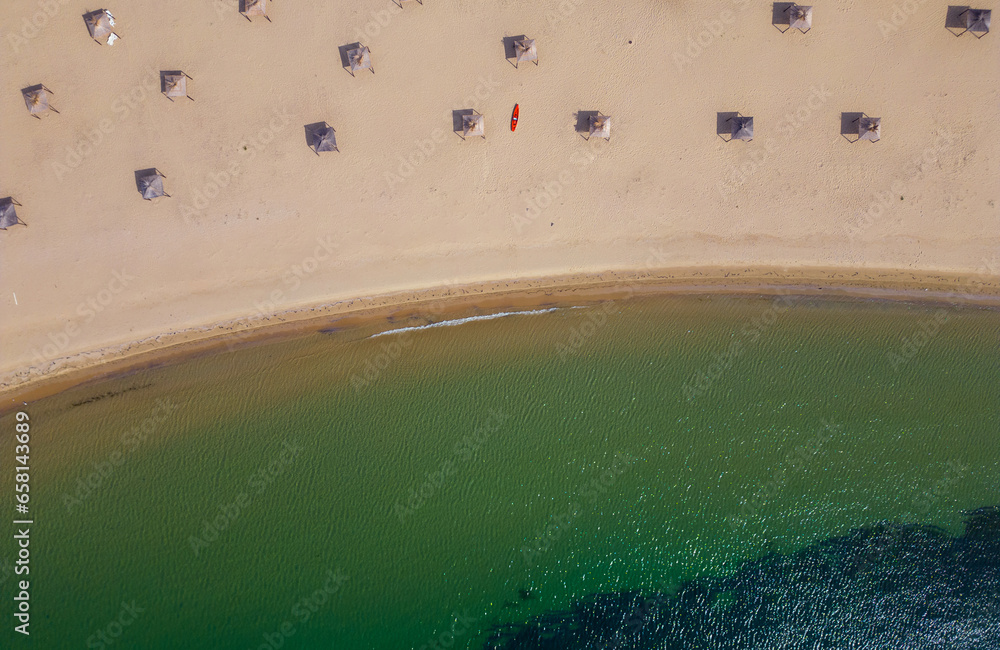 aerial view of a sandy deserted beach with straw umbrellas, a red sea kayak and a calm turquoise sea