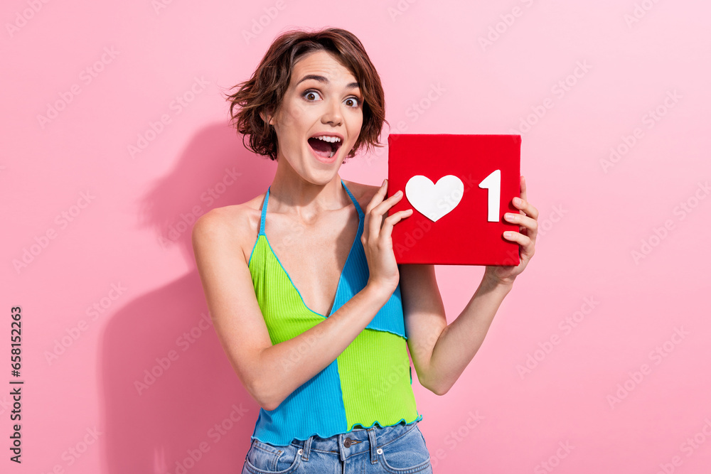 Photo of impressed excited lady wear green blue tank top holding heart like card isolated pink color background Photo of impressed excited lady wear green blue tank top holding heart like card isolated pink color background