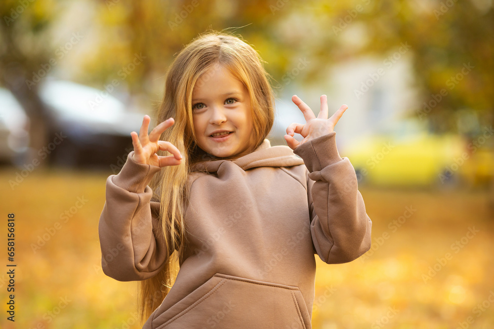 Happy little child girl laughing and playing in the autumn on the nature walk over fallen leaves outdoors. Autumn season. Happy child over nature background at city street. Happy little child girl laughing and playing in the autumn on the nature walk over fallen leaves outdoors. Autumn season. Happy child over nature background at city street.