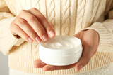 Jar of cream in female hands on light background, close up