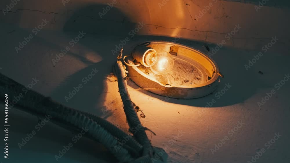 An incandescent light bulb glows in an old broken lamp on the concrete