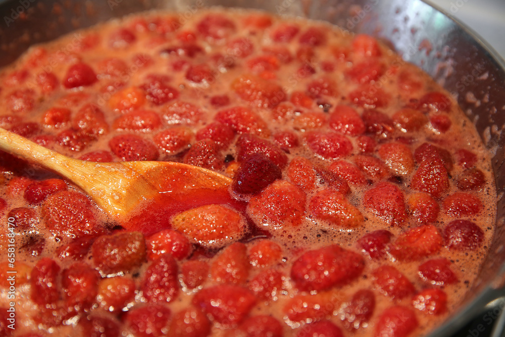Cooking strawberry jam in a large bowl at home. Wooden spoon in a bowl with jam Cooking strawberry jam in a large bowl at home. Wooden spoon in a bowl with jam