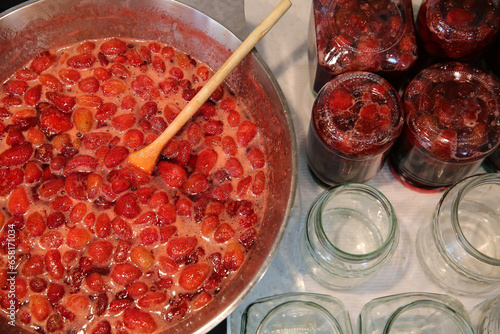 Cooking strawberry jam in a large bowl at home. Wooden spoon in a bowl with jam. Empty glass jam jars and jars filled with jam.