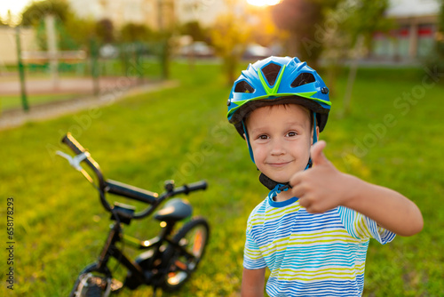 Toddler boy in helmet after bike ride. Sport lifistyle kids. Child active outdoor. Bicycle on the green grass.
