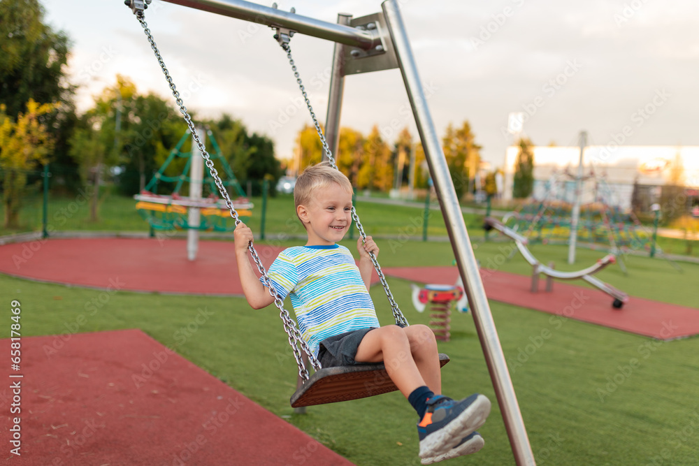 A child is playing in an outdoor playground. Children play in the yard of the kindergarten. Active boy on a swing. Health summer spring activity for children on a summer day. A little boy is swinging.