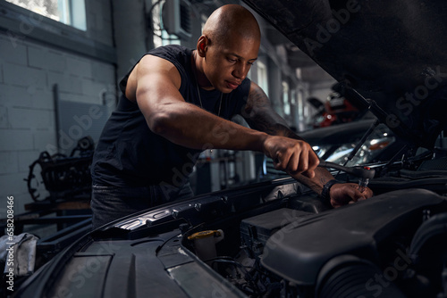 Masculine African American auto-mechanic checking sparking plugs in car © Viacheslav Yakobchuk