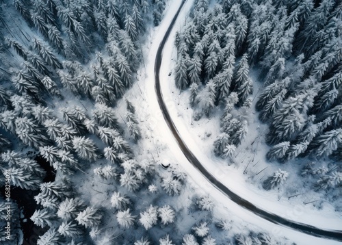 an aerial shot of snowy road in the middle of a forest © olegganko