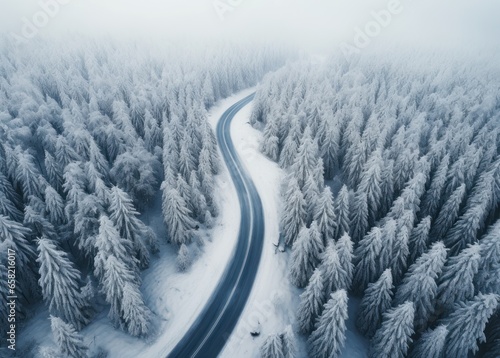 an aerial shot of snowy road in the middle of a forest