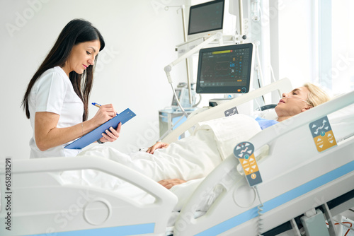 Pleasant nurse recording the patients vital signs
