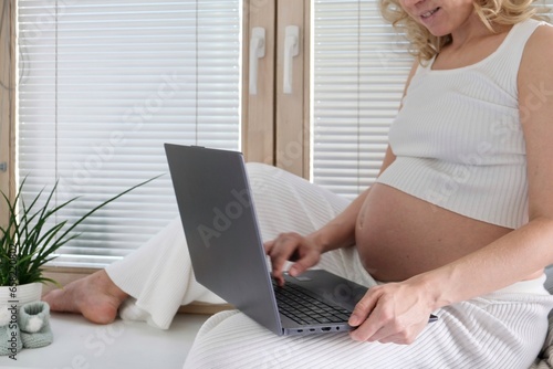 A young pregnant woman is working on a laptop. Pregnant freelancer. Portrait young pregnancy woman using online laptop