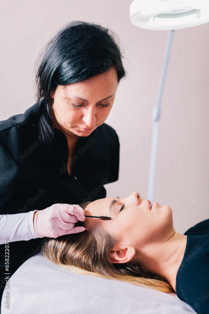 Fototapeta premium Beautician styling eyebrow shape and design on her client's face in a beauty salon