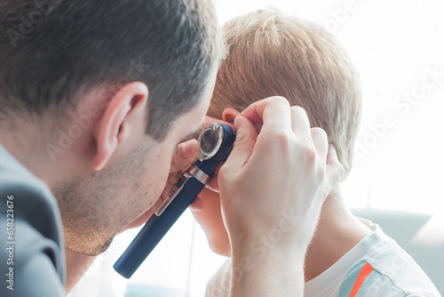 A child with earache at the hospital. Doctor otolaryngologist checking child ears in the hospital. Cute boy with bad ears at the doctor's office in the clinic. photo