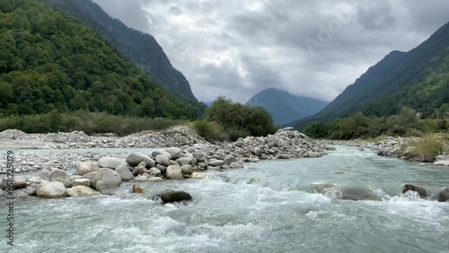Panoramic view of a mountain river with stones and a mountain with green forests on a cloudy fall day. photo