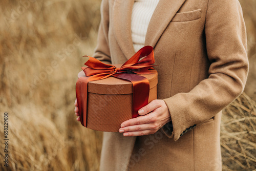 Hands of woman holding gift box in field photo
