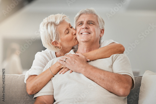 Happy senior couple  kiss and hug on sofa in living room for embrace  love or affection at home. Mature woman kissing and hugging man with smile in care  trust or support on lounge couch in house
