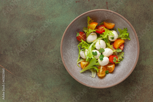 Salad with lettuce, mozzarella and tomatoes in a plate on the table. Caprese salad. Top view