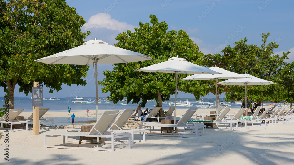 sandy beach with comfortable sun beds and umbrellas on a tropical island, on a sunny day, calm