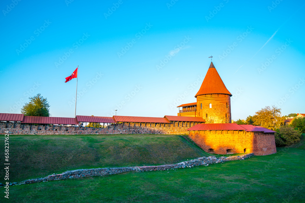Lithuania, Kaunas castle building and flag in warm sunset light, ancient red brick wall and tower