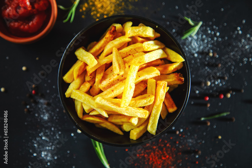 French fries with ketchup and spices on a black background.