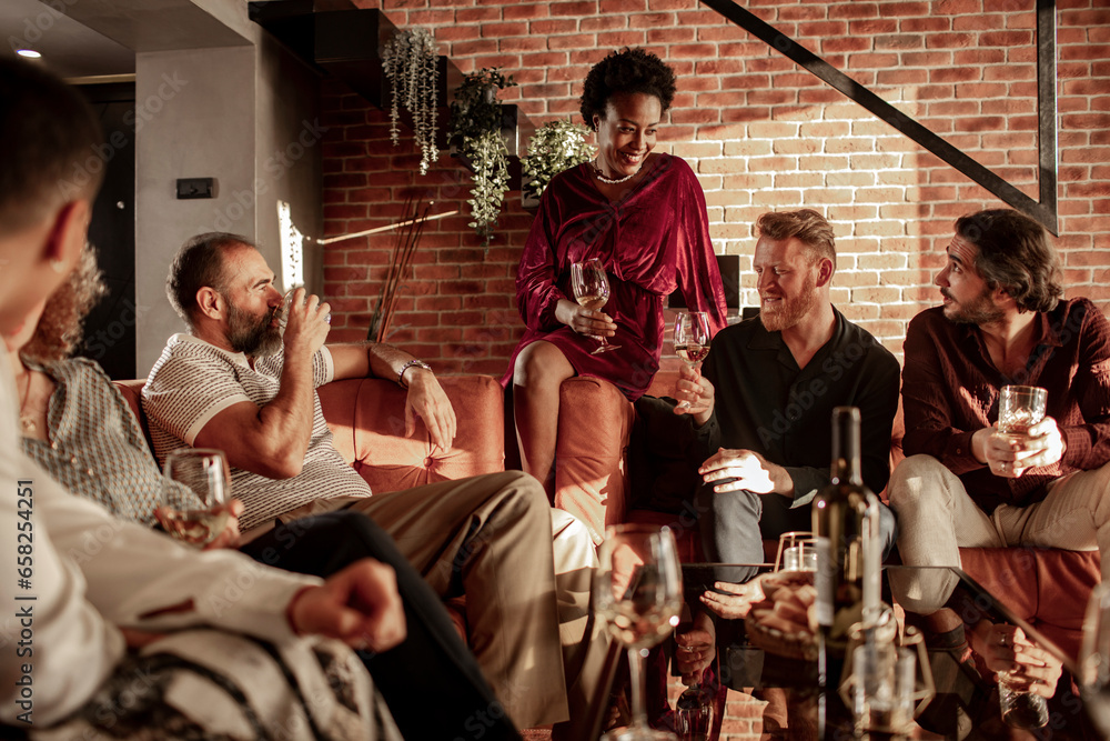 Diverse age group of friends having a conversation over some drinks on the couch at home Diverse age group of friends having a conversation over some drinks on the couch at home