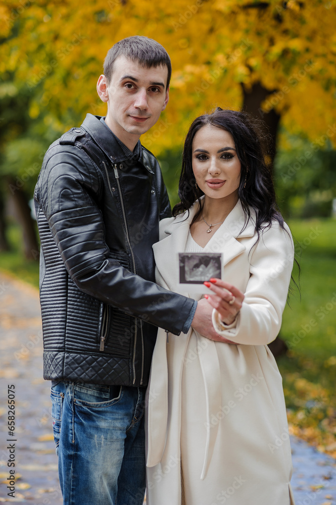 Fototapeta premium A man hugs his pregnant wife. Woman holding ultrasound photo of baby