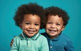 Two joyful children laughing against a teal background.