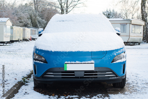 Blue electric car with green numberplate stripe with snow on the bonnet