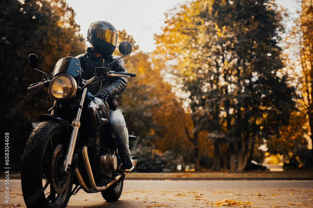 motorcyclist in a helmet with a classic motorcycle in the fall. Stylish motorcyclist in a leather jacket and gloves.