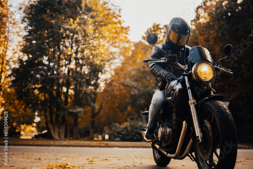 motorcyclist in a helmet with a classic motorcycle in the fall. Stylish motorcyclist in a leather jacket and gloves.