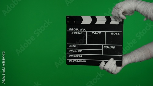 Detail green screen isolated chroma key photo capturing mummy's hands holding a director's film movie slateboard, clapper board.