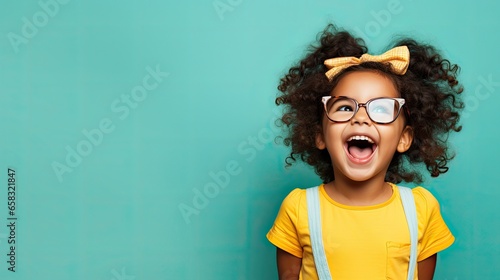 Laughing child with curly hair and glasses on a teal background.