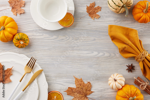 Set up a table for a memorable Thanksgiving. Top view flat lay of plates, cutlery, cup, orange napkin, pumpkins, seasonal attributes on light wooden background with advert zone