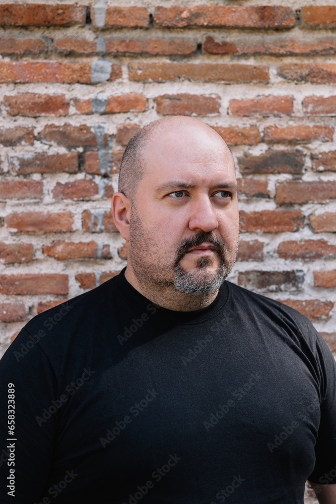 Exterior close-up of a 45-year-old bald man with a goatee and mustache looking to the right against a brick background Exterior close-up of a 45-year-old bald man with a goatee and mustache looking to the right against a brick background