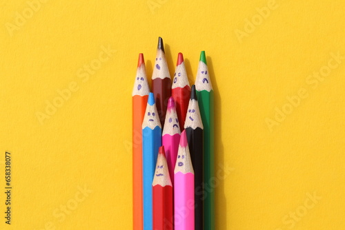 Multi-colored pencils with painted faces lie on a yellow background.	