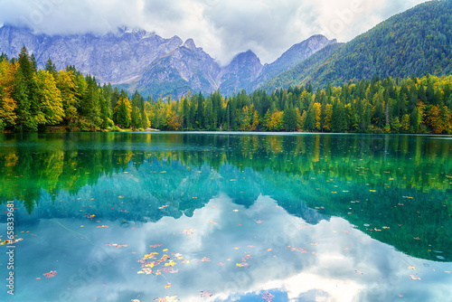 Laghi di Fusine inferior lake, Tarvisio, Italy. Amazing autumn landscape, crystal clear water with reflection and colored forest surrounded by Mangart mountain range, outdoor travel background photo