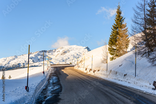 Deserted stretch of a mountain pass road between snowy slopes on a sunny winter day