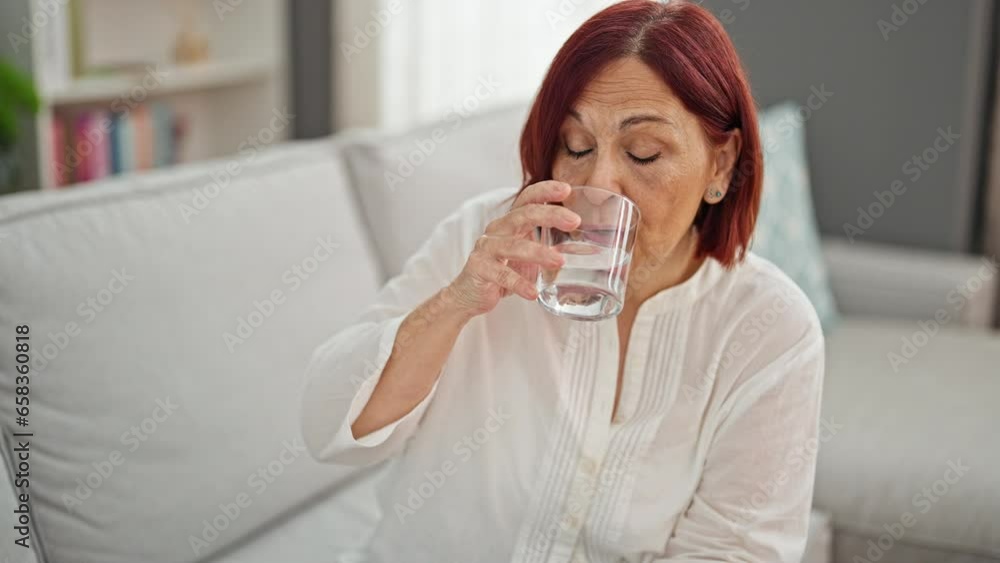 Middle age woman drinking glass of water sitting on sofa speaking at home Middle age woman drinking glass of water sitting on sofa speaking at home